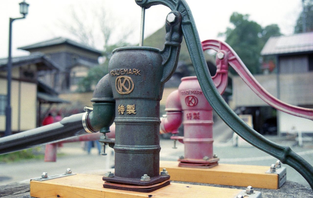Close-up of a vintage water pump in a traditional Japanese setting, showcasing rustic charm.
